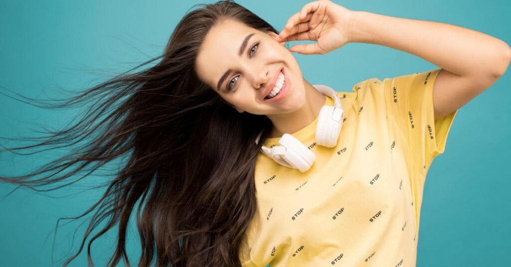 Portrait of a smiling woman wearing headphones, with her long hair flowing against a turquoise background.